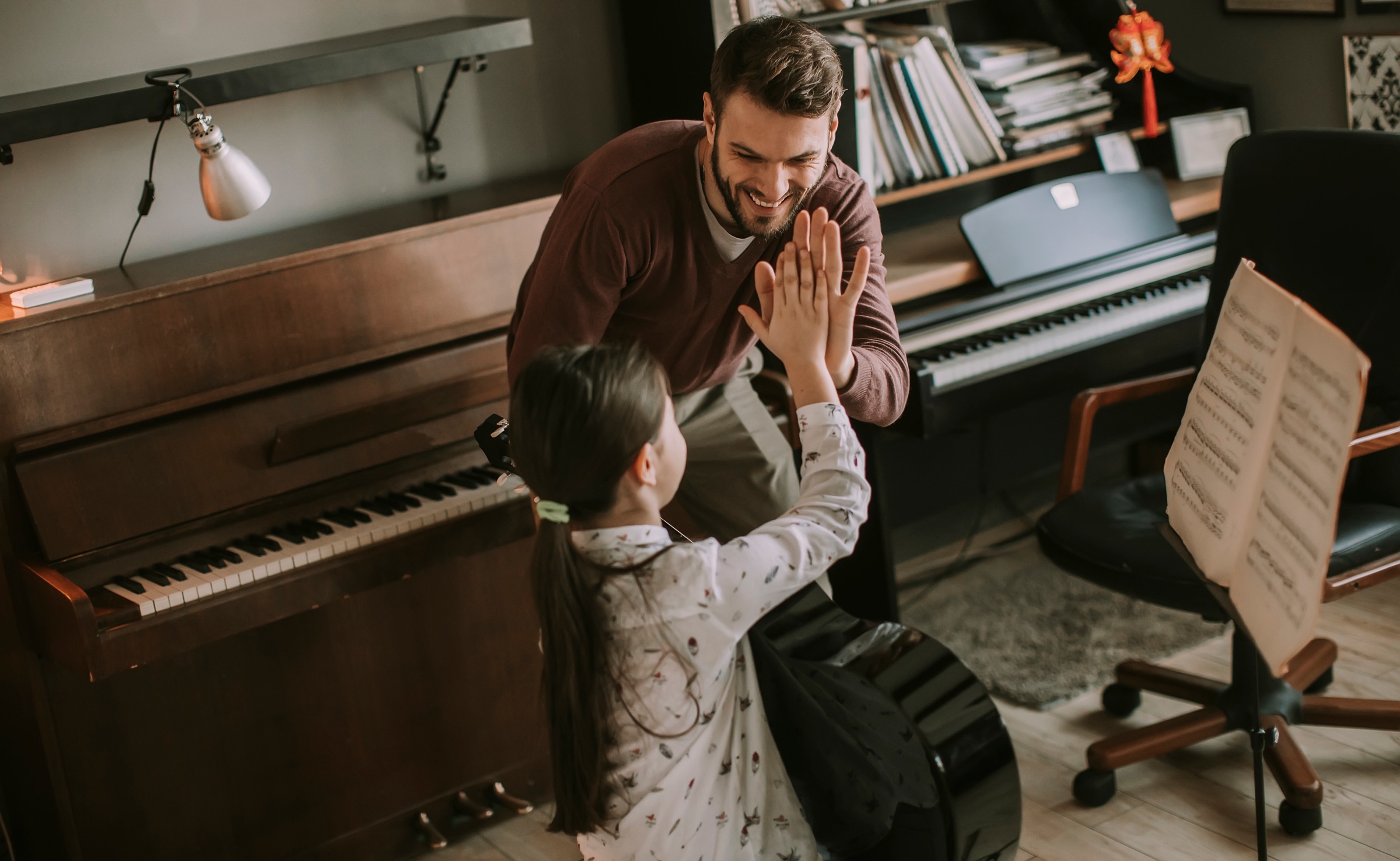 A music teacher and young student high-five during a piano lesson